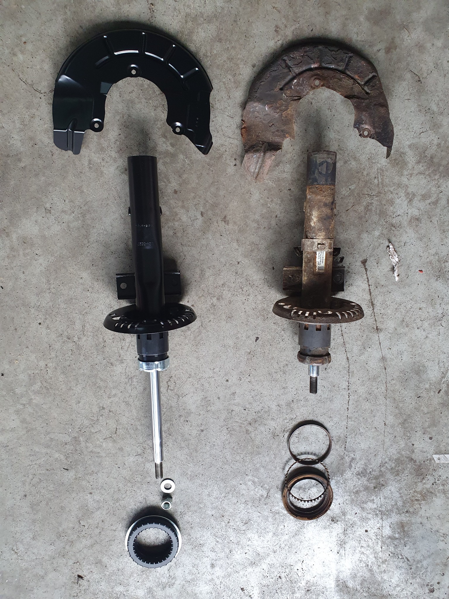 Porównanie nowego i zużytego amortyzatora samochodowego z osłoną tarczy hamulcowej, widoczne ślady korozji na starym elemencie.