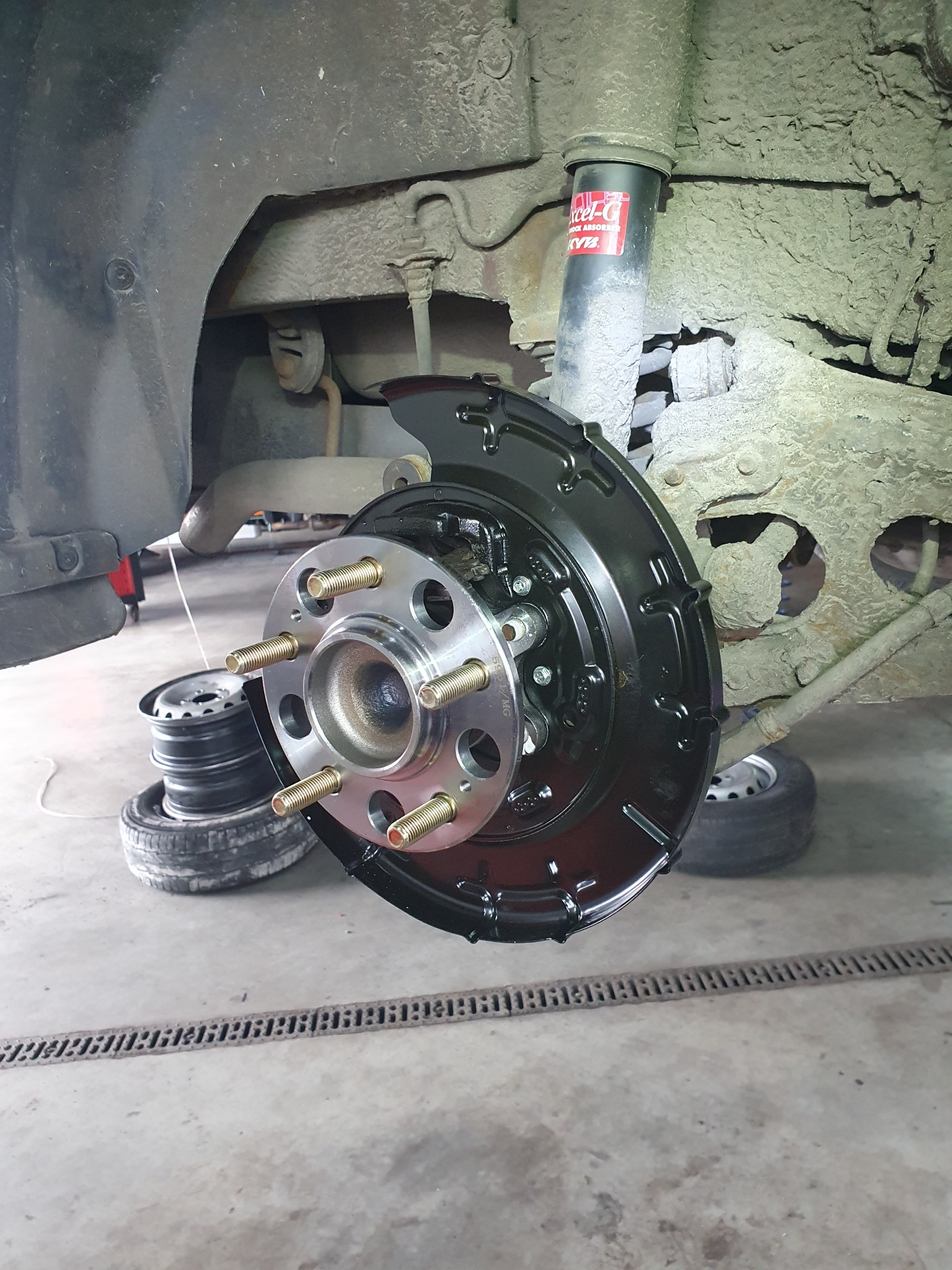 Nowa tarcza hamulcowa z piastą, zamontowana w samochodzie w warsztacie w Oświęcimiu. Widoczne ślady korozji na elementach zawieszenia i amortyzator KYB.