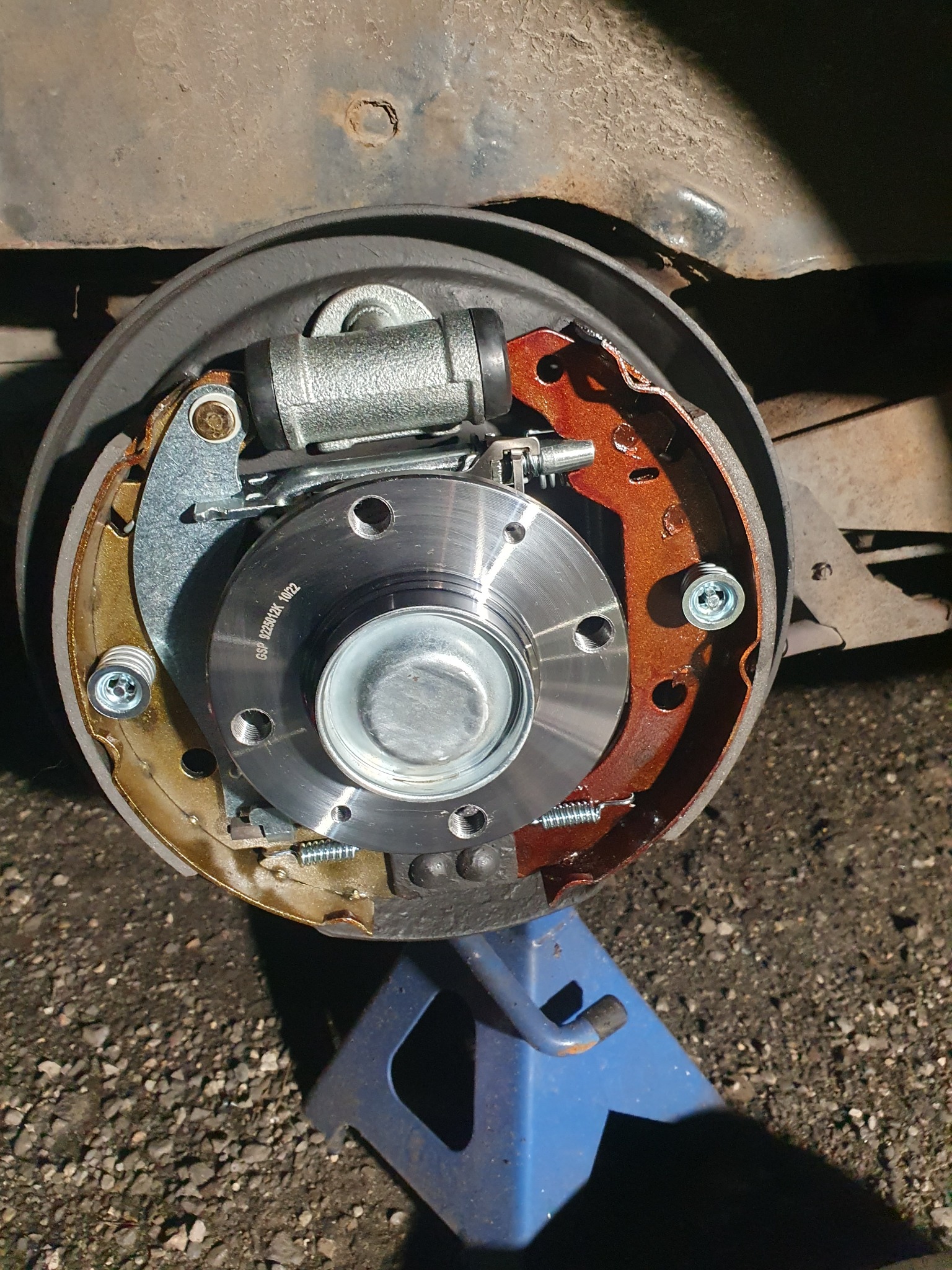 Nowe szczęki hamulcowe bębnowe zamontowane na piaście, widoczny cylinder hamulcowy i sprężyny, auto na podnośniku warsztatowym.