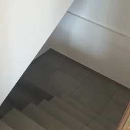 Wykończone schody wewnątrz budynku, pokryte szarą, kwadratową glazurą, widok z góry, surowa żarówka na suficie.