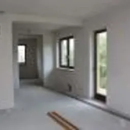 Wnętrze pomieszczenia po nałożeniu gładzi gipsowej, widoczne okna i drzwi, jasne ściany i podłoga, minimalne ślady prac wykończeniowych.