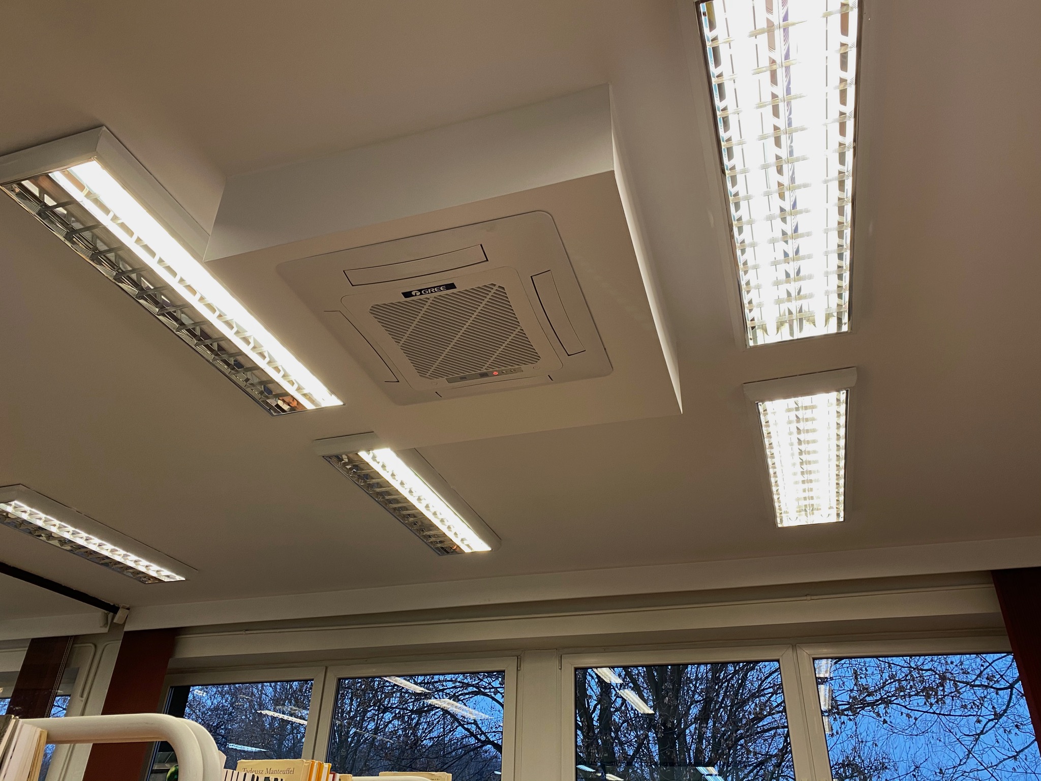 Sufit z zamontowaną kasetonową klimatyzacją Gree i oświetleniem rastrowym, widok od dołu.