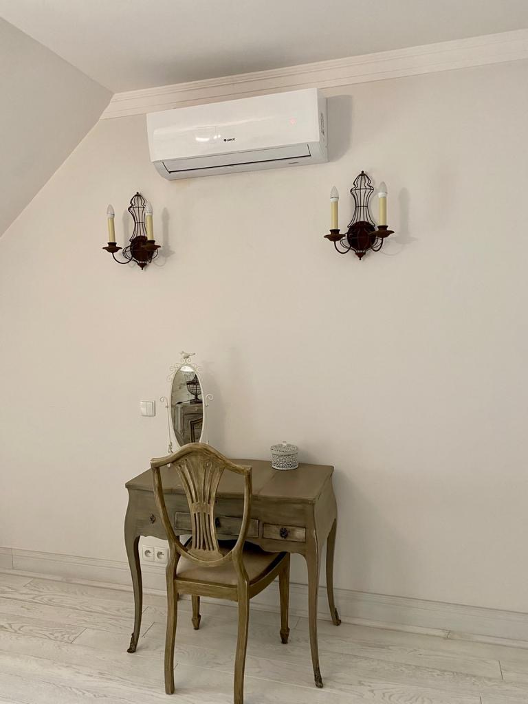 Biały klimatyzator Gree zamontowany nad toaletką w stylu vintage z lustrem i świecznikami na ścianie.