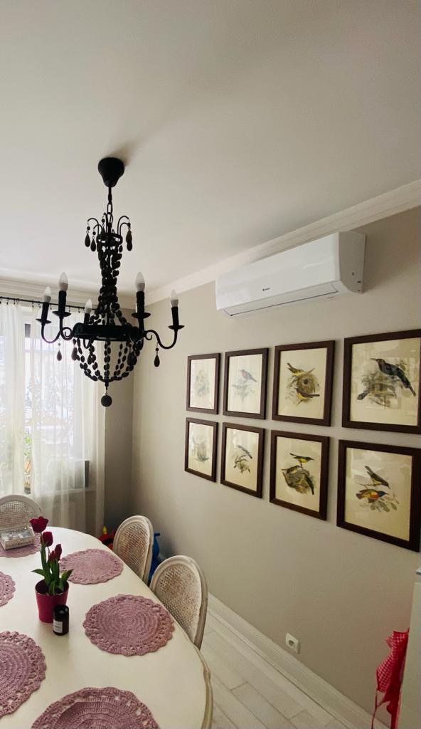 Wnętrze jadalni z zamontowanym klimatyzatorem ściennym, czarny żyrandol z koralikami, obrazy z ptakami na ścianie i stół z dekoracjami.