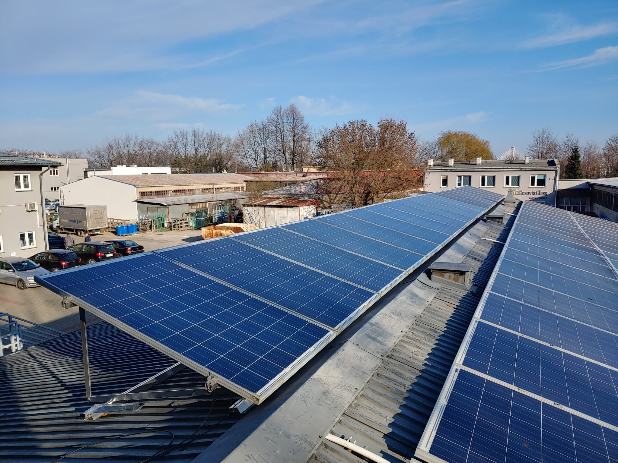 Instalacja paneli fotowoltaicznych na dachu budynku przemysłowego, widok z góry, błękitne niebo w tle.