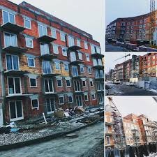 Nowo budowany budynek wielorodzinny z widocznymi oknami na różnych etapach montażu, z perspektywy ulicy, w tle dźwig budowlany.