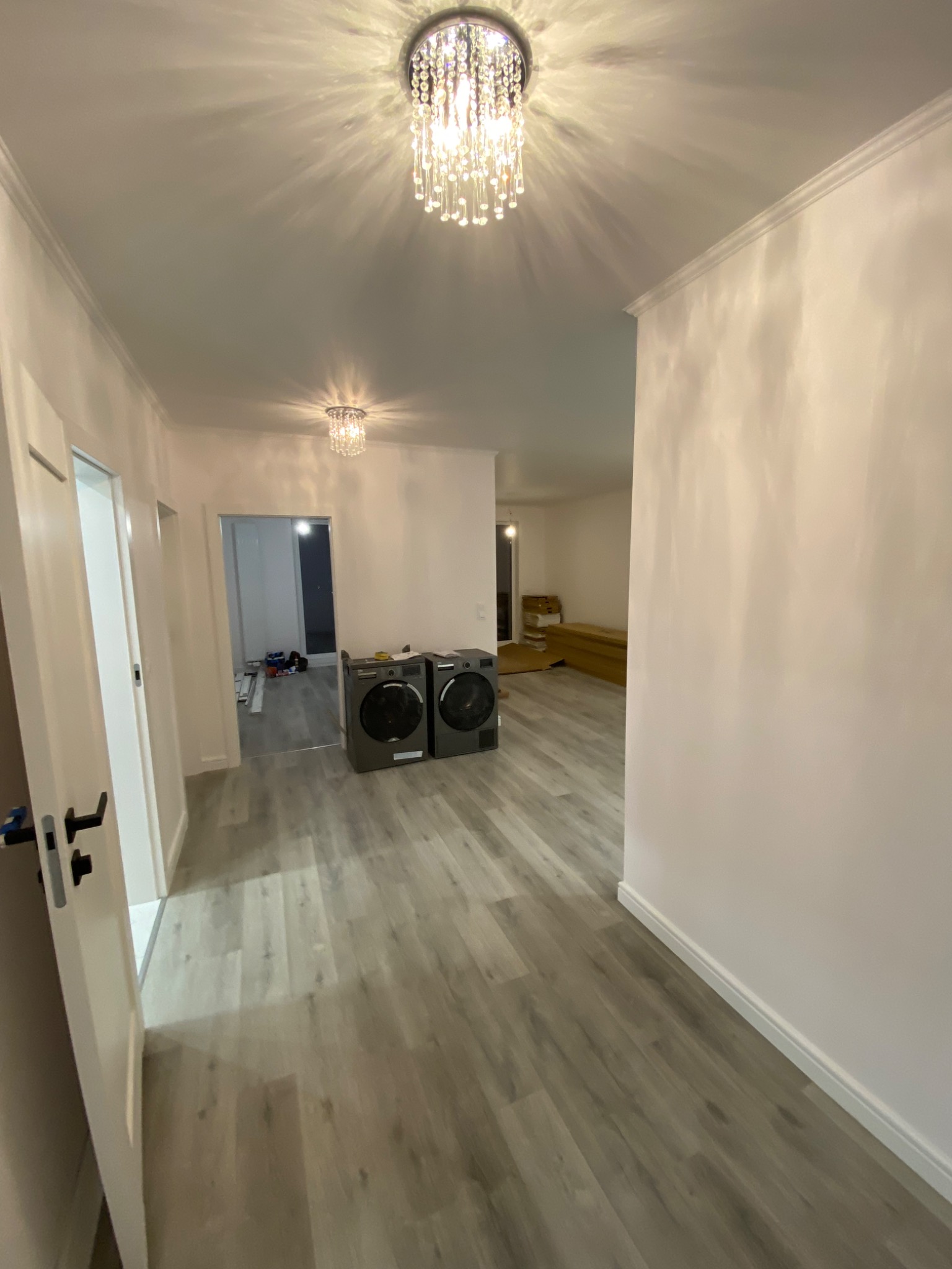 Wykończone wnętrze mieszkania z panelami podłogowymi w odcieniach szarości, świeżo pomalowanymi ścianami, ozdobną listwą przysufitową i dwoma nowoczesnymi oczyszczaczami powietrza w tle.