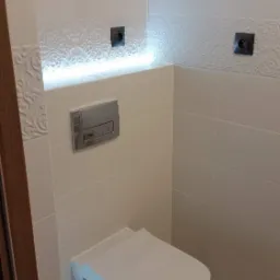 Nowoczesna toaleta podwieszana w jasnej łazience z dekoracyjną listwą oświetleniową LED i gniazdkami elektrycznymi.