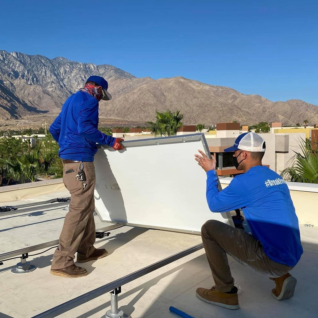 Dwóch instalatorów w Nevadzie montuje panel fotowoltaiczny na dachu budynku z widokiem na góry w słoneczny dzień.