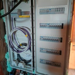 Piorun Piotr Szojda - Rozdzielnica elektryczna Hager w trakcie montażu, widoczne kable i zabezpieczenia. Ściana wokół zabezpieczona pianką montażową. Detal instalacji elektrycznej.