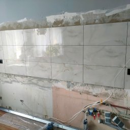 Piorun Piotr Szojda - Położone płytki imitujące marmur na ścianie z gniazdkami, widoczne instalacje hydrauliczne i elektryczne w trakcie prac wykończeniowych.