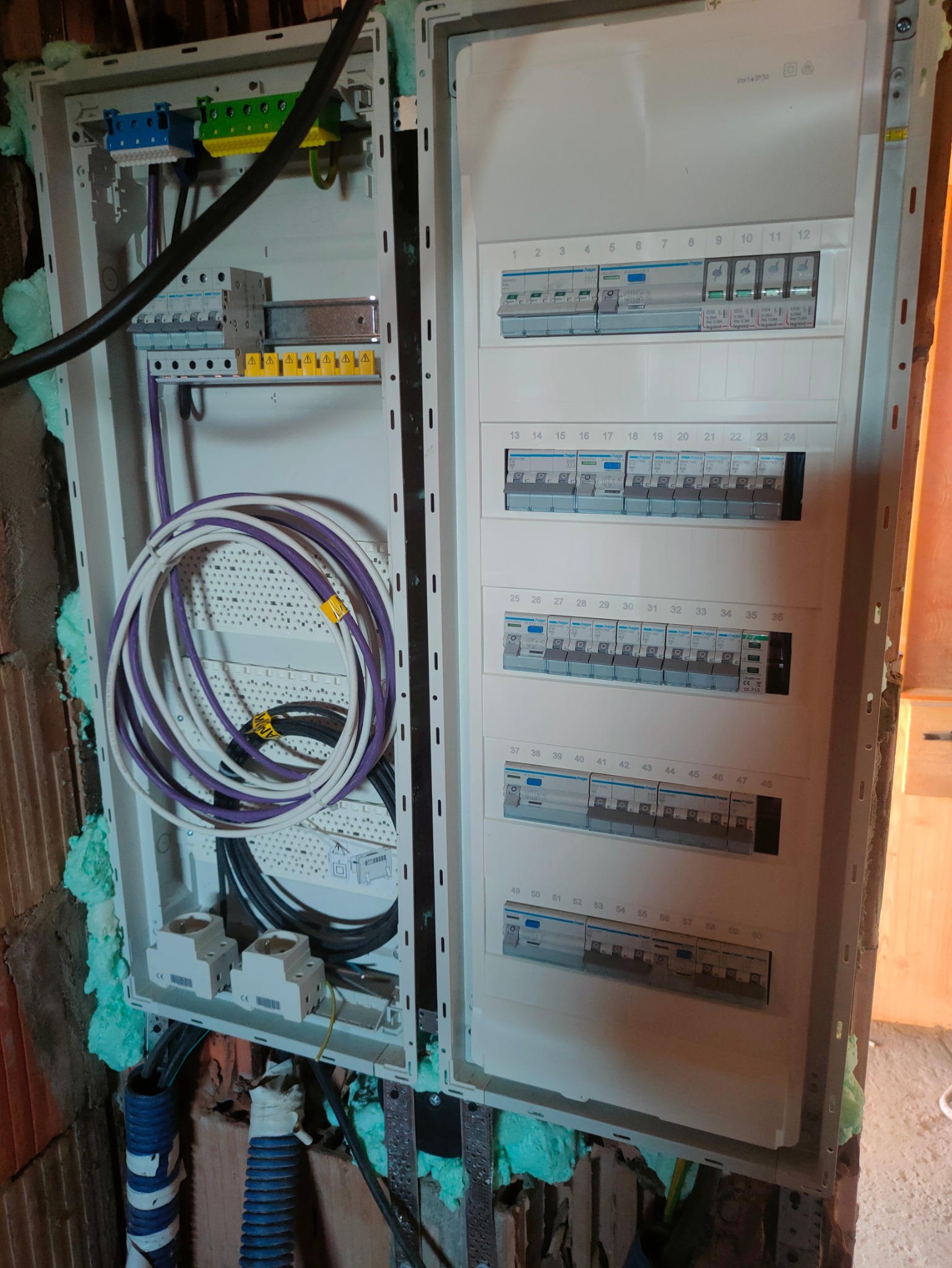 Rozdzielnica elektryczna Hager w trakcie montażu, widoczne kable i zabezpieczenia. Ściana wokół zabezpieczona pianką montażową. Detal instalacji elektrycznej.