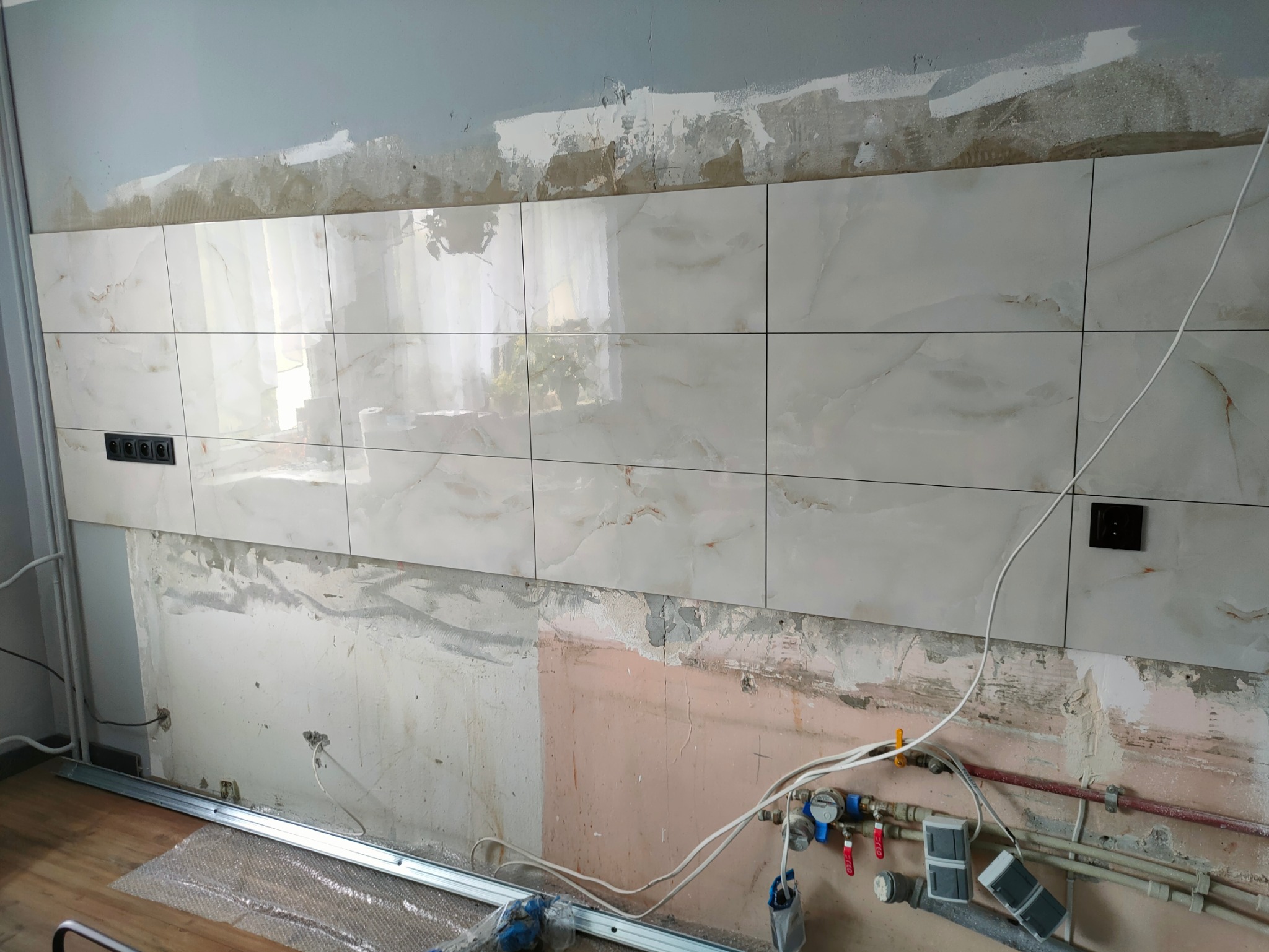 Położone płytki imitujące marmur na ścianie z gniazdkami, widoczne instalacje hydrauliczne i elektryczne w trakcie prac wykończeniowych.