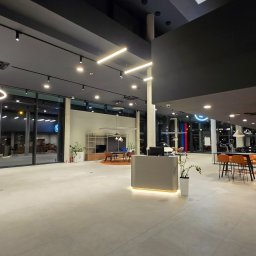 IdealSpace Sp. z o.o. - Nowoczesny salon samochodowy BMW po remoncie: minimalistyczny design, jasne oświetlenie, szklane witryny, recepcja z podświetleniem LED, eleganckie meble i ekspozycja aut.