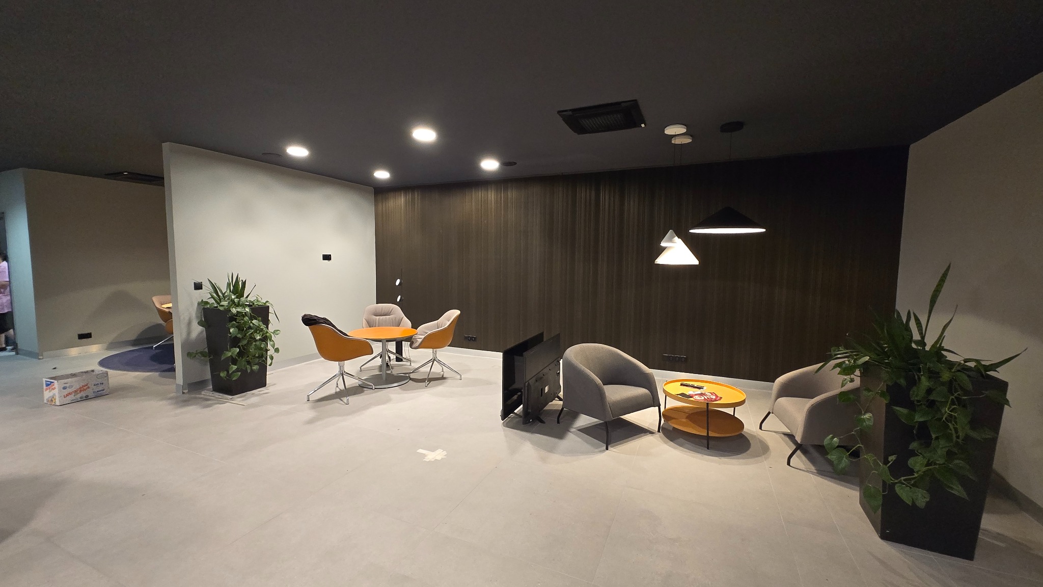 Nowoczesne wnętrze salonu samochodowego po remoncie: szare płytki, ciemne ściany, designerskie lampy i meble w strefie relaksu. Widoczne rośliny w donicach.