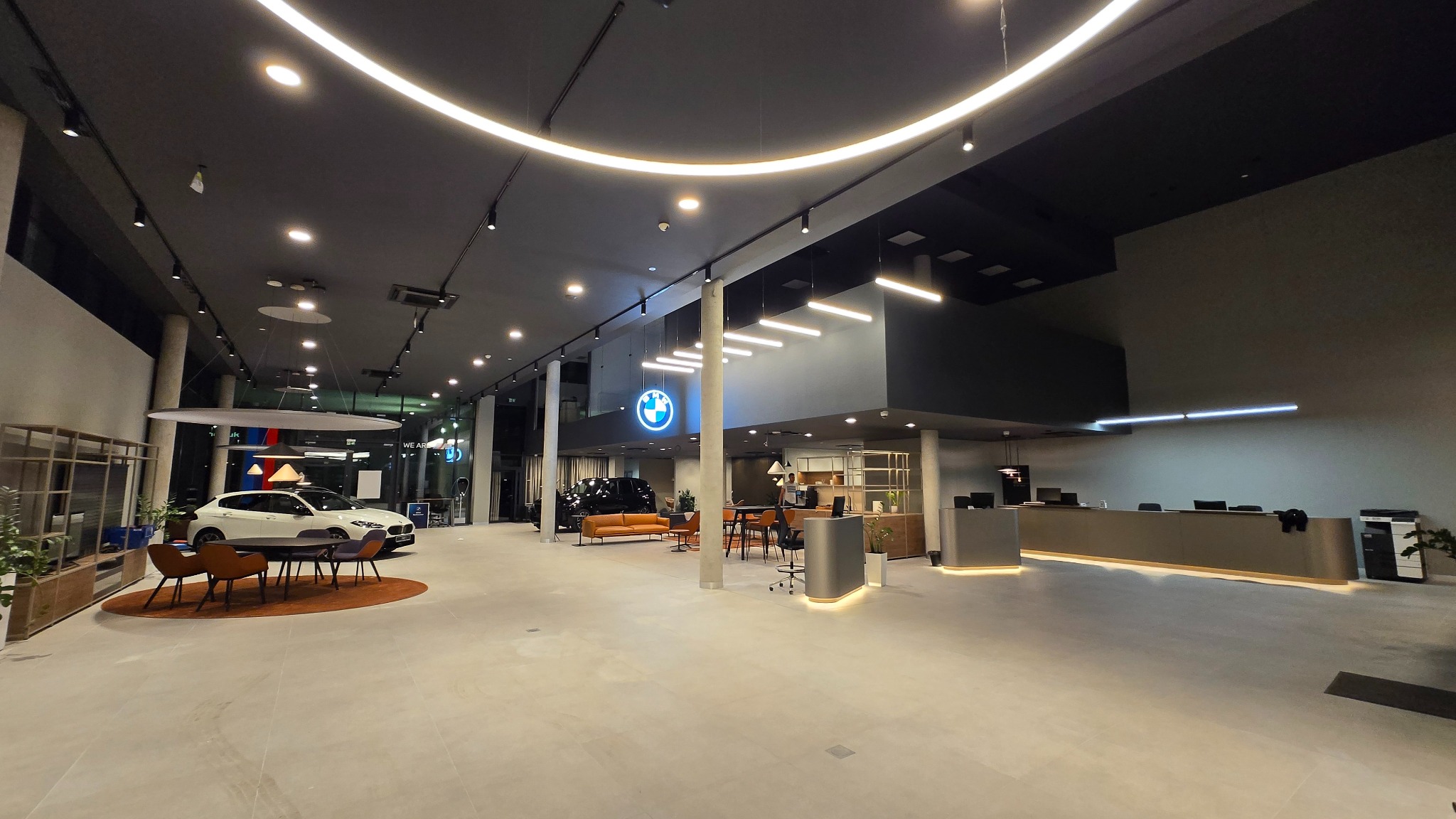 Salon BMW po remoncie: jasne wnętrze z nowoczesnym oświetleniem, eksponowane samochody, recepcja i strefa klienta. Widok na przestrzeń salonu z perspektywy szerokokątnej.