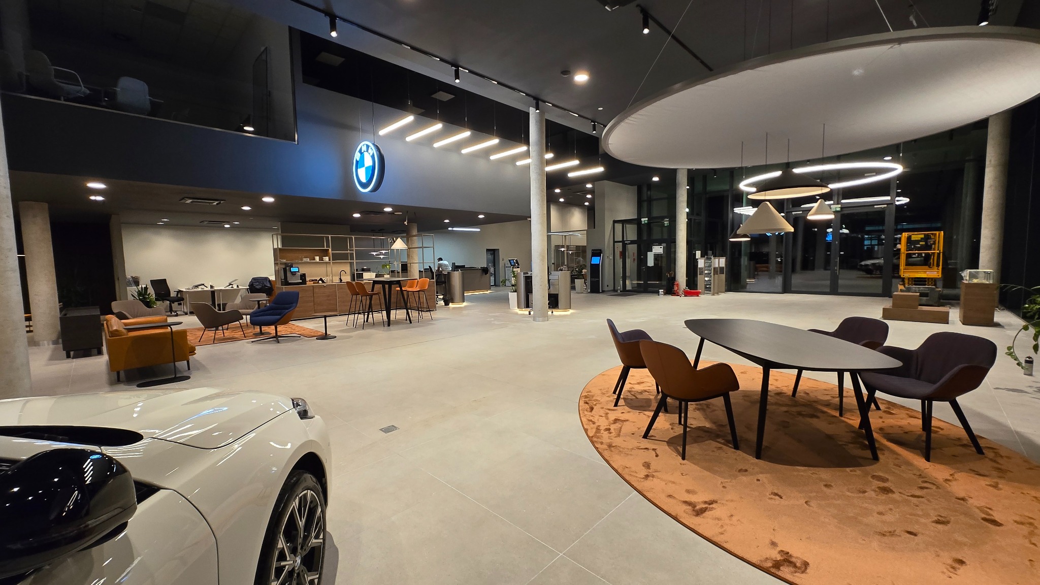 Przestronne wnętrze salonu samochodowego BMW po remoncie: nowoczesny design, oświetlenie LED, meble designerskie, widoczny fragment białego auta.