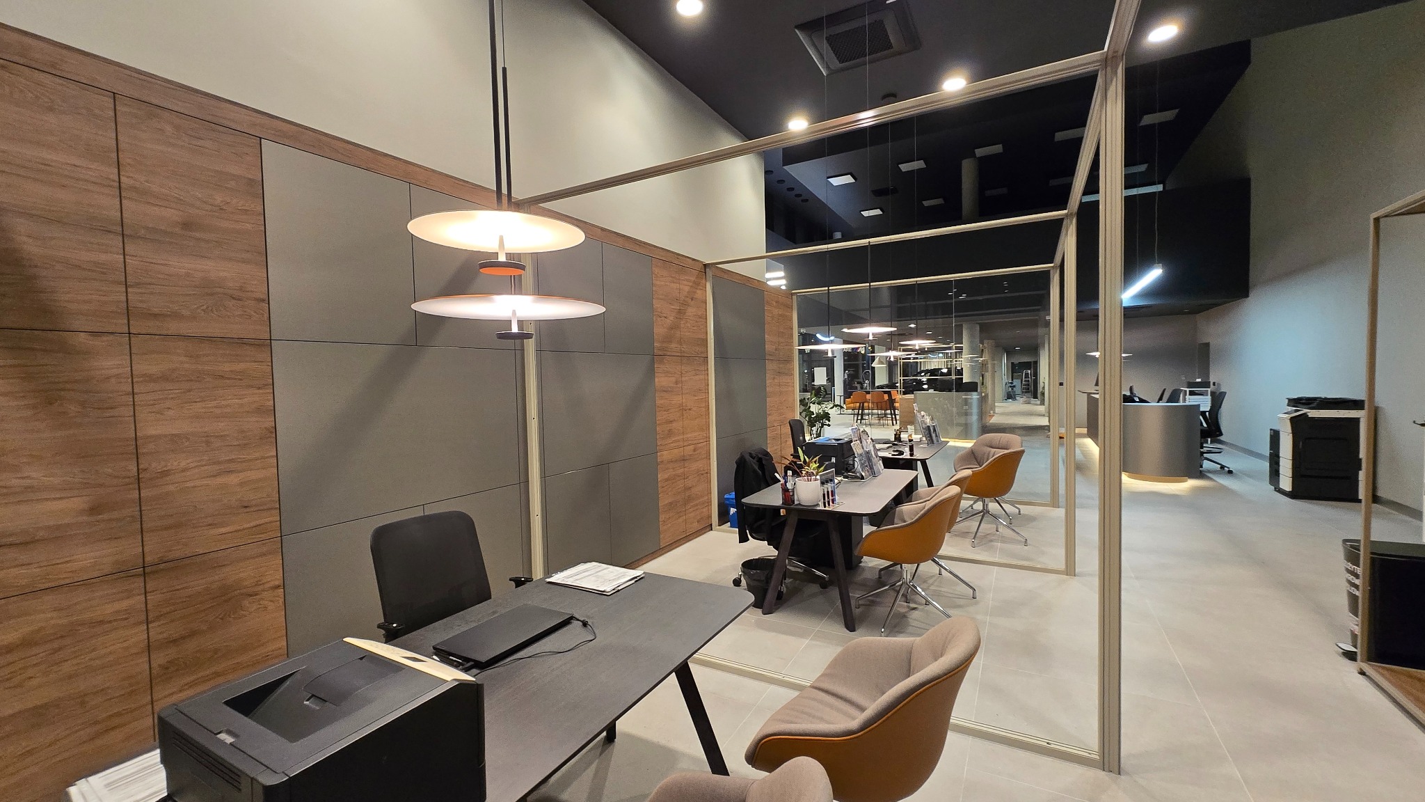 Nowoczesne biuro po remoncie: szklane ścianki działowe, designerskie lampy, drewniane panele ścienne. Widok na przestrzeń biurową z biurkami i krzesłami.