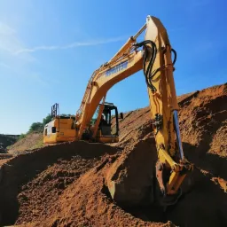 Żółta koparka Komatsu nabiera brązową ziemię z hałdy na tle błękitnego nieba.