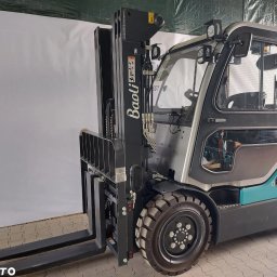 Grupa PGS Sp. z o.o. - Nowy wózek widłowy spalinowy Baoli w kolorze szaro-turkusowym, z widocznym logo marki na maszcie, prezentowany na tle białej ściany w pomieszczeniu.