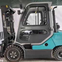 Niebiesko-szary wózek widłowy marki Baoli, widok z boku, z widoczną kabiną operatora, oponami i masztem, na tle białej ściany.