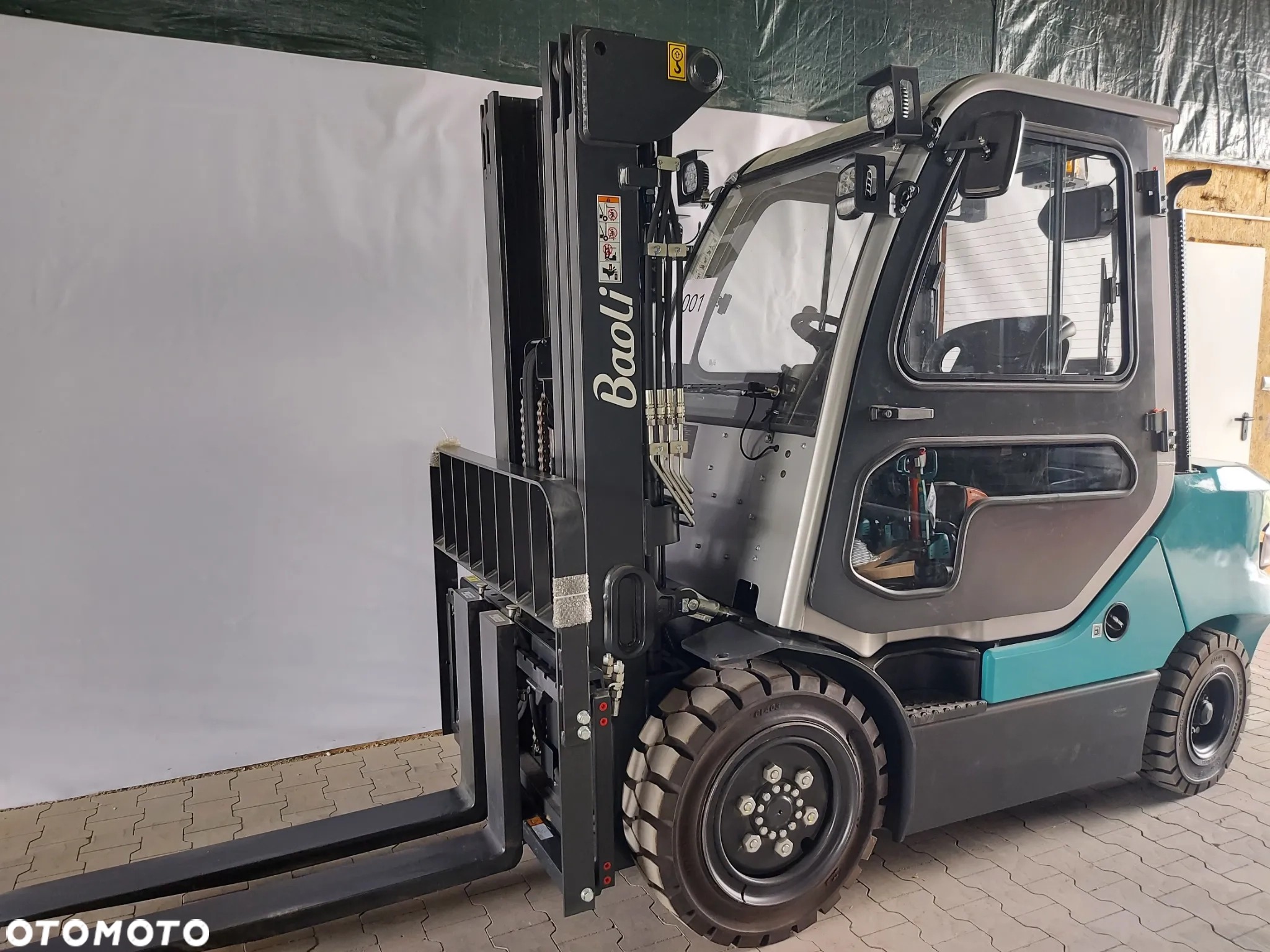 Nowy wózek widłowy spalinowy Baoli w kolorze szaro-turkusowym, z widocznym logo marki na maszcie, prezentowany na tle białej ściany w pomieszczeniu.