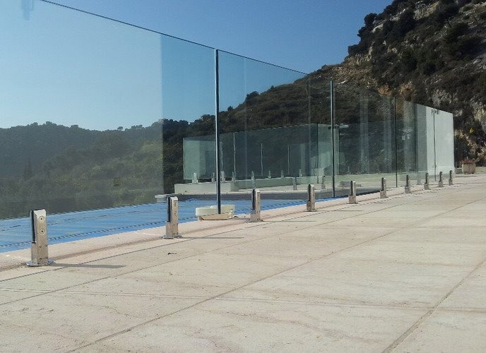 Szklana bariera ochronna z metalowymi słupkami na betonowym tarasie z widokiem na wzgórza.