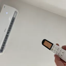 Biały klimatyzator marki Rotenso zamontowany na suficie, sterowany pilotem ustawionym na 16 stopni Celsjusza.