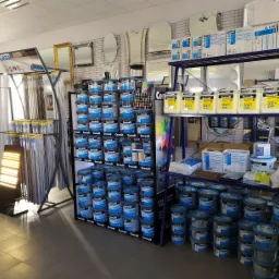 Wnętrze sklepu budowlanego z ekspozycją materiałów wykończeniowych: farby, kleje, fugi marki Ceresit oraz profile wykończeniowe Cezar, lustra i akcesoria łazienkowe.