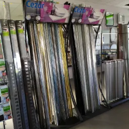 Ekspozycja profili wykończeniowych Cezar w sklepie, różne kolory i rodzaje, w tle lustra i inne akcesoria łazienkowe.