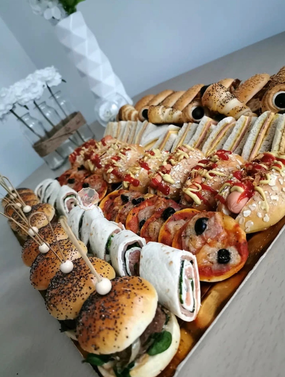 Elegancki catering: taca z mini burgerami na szpilkach, roladkami w tortilli z łososiem, mini pizzami z oliwkami, hot dogami w bułce z sosem i posypką, kanapkami oraz słonymi paluchami.