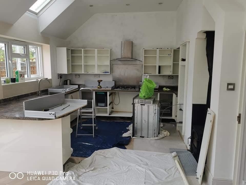 Wnętrze kuchni w trakcie montażu mebli: widoczne szafki bez frontów, sprzęt AGD, drabina i narzędzia. Przygotowanie do instalacji kuchni na wymiar.