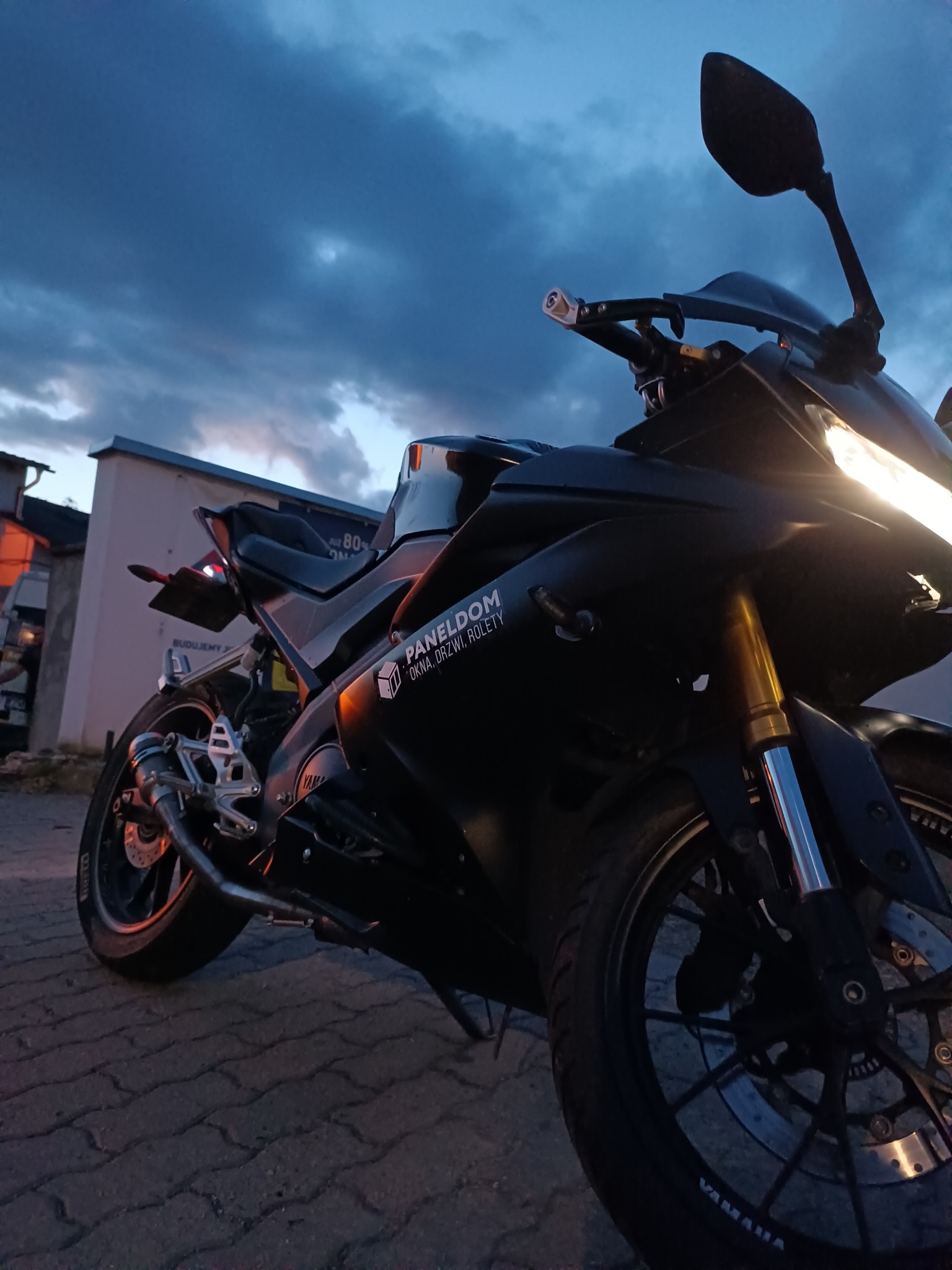 Czarny motocykl z naklejką firmy budowlanej na tle zachmurzonego nieba.