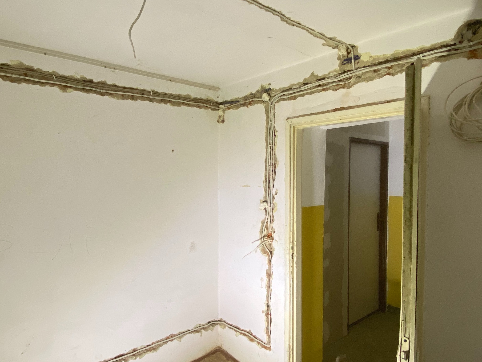 Surowe wnętrze pokoju w trakcie remontu z widocznymi przewodami elektrycznymi prowadzonymi w bruzdach w ścianach i suficie, przygotowanymi do dalszych prac wykończeniowych.