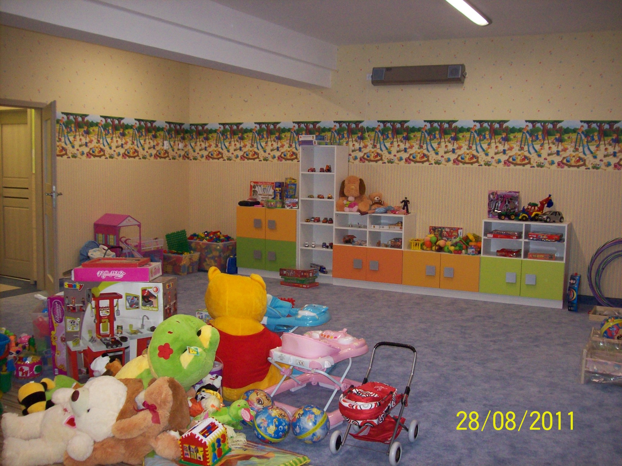 Pokój dziecięcy z kolorowymi meblami, zabawkami i dekoracyjnym paskiem na ścianie z motywem placu zabaw.