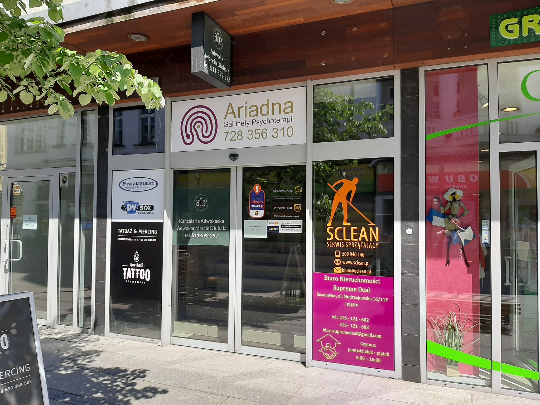 Fasada budynku z szyldem 'Ariadna Gabinety Psychoterapii' nad wejściem, obok szyldy innych firm, widok z zewnątrz.