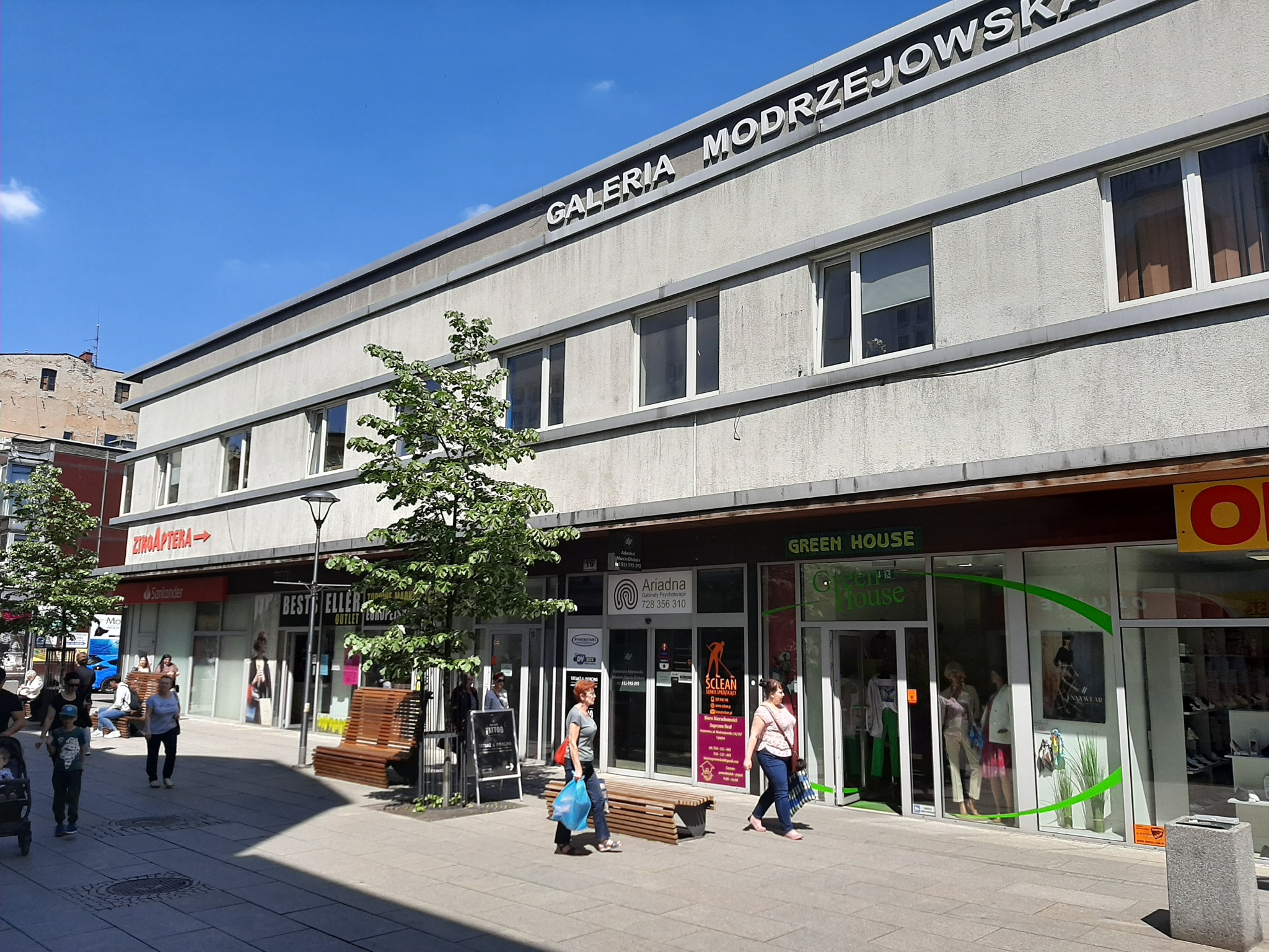 Fasada budynku Galerii Modrzejowska z licznymi lokalami usługowymi, w tym gabinetem psychoterapii Ariadna, widok z chodnika w słoneczny dzień.