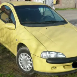 Żółty Opel Tigra z 1997 roku, sfotografowany na zewnątrz w słoneczny dzień, z widocznym rowerem w tle i elementami muru.