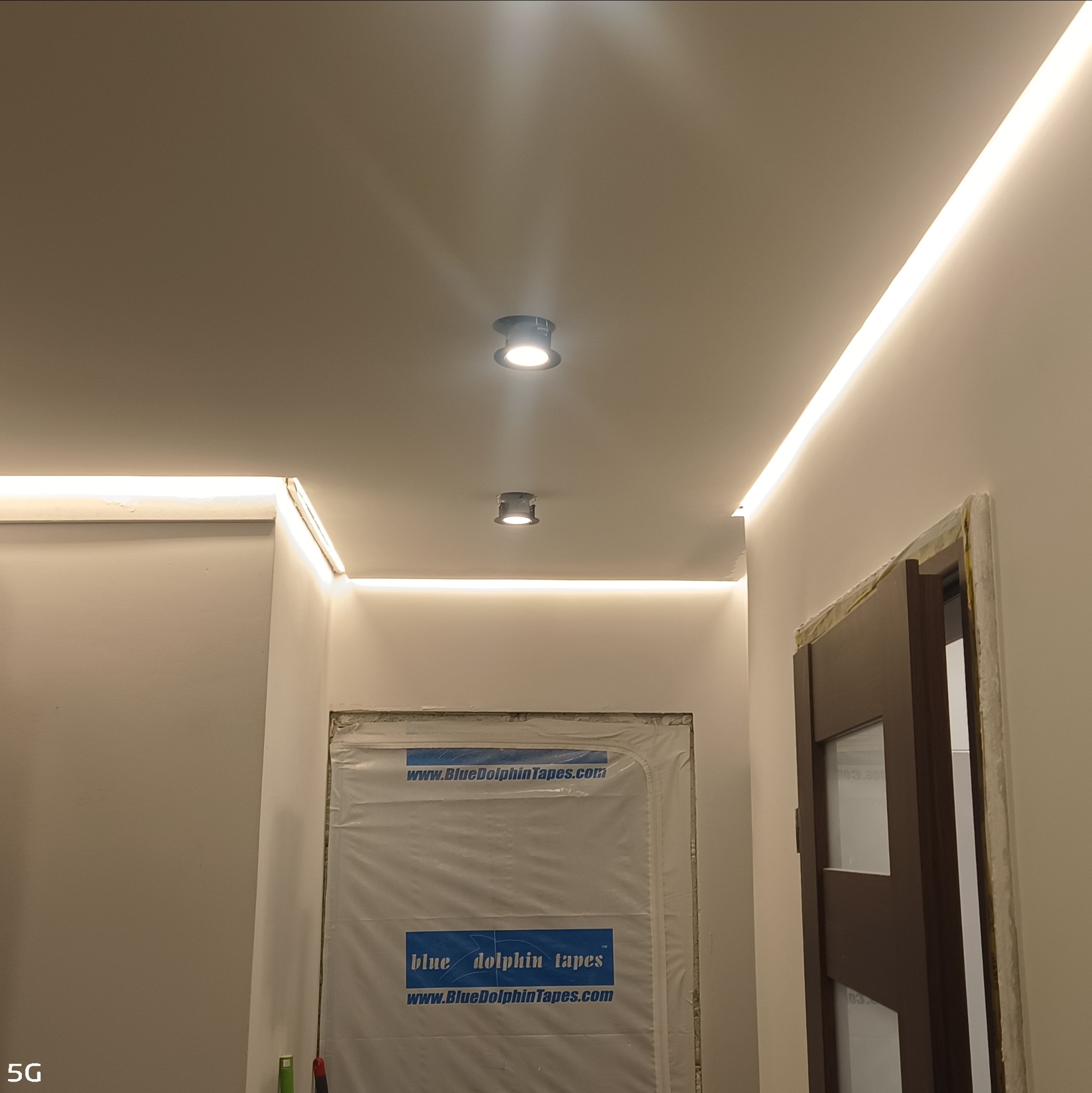 Nowoczesne oświetlenie sufitowe z listwami LED i dwoma punktowymi lampami w jasnym wnętrzu. Drzwi z częściowo osłoniętą futryną w tle.