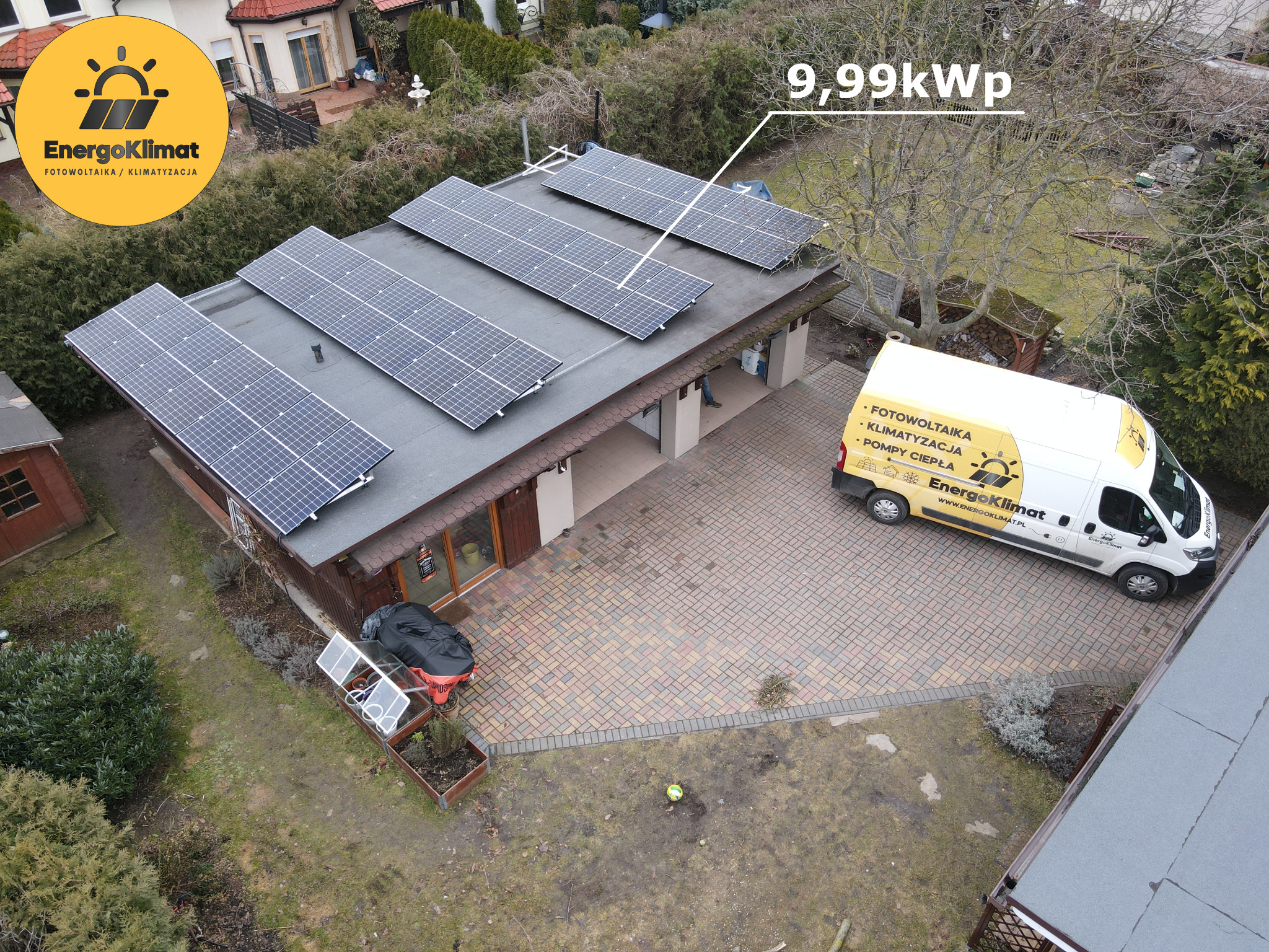 Widok z góry na dom z panelami słonecznymi o mocy 9,99kWp na dachu, obok zaparkowany biały samochód dostawczy z logo firmy, na ziemi mała szklarnia i zabawka dla dziecka.