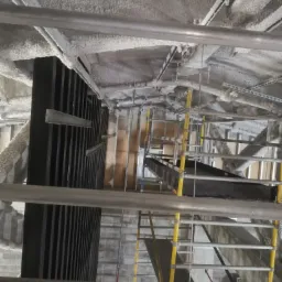 Sufit z widoczną konstrukcją i nałożoną pianą izolacyjną, widok z rusztowania, elementy instalacji pod sufitem.