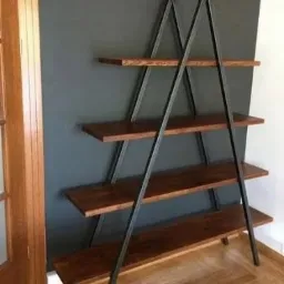 Regał drabinkowy z czterema drewnianymi półkami i metalową, czarną konstrukcją w kształcie litery A, ustawiony na parkiecie w pomieszczeniu z szarą ścianą.