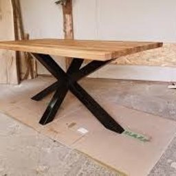 Emil Gradzik - Stół z blatem z jasnego drewna i czarną, metalową podstawą w kształcie litery X, umieszczony na kartonie w warsztacie.