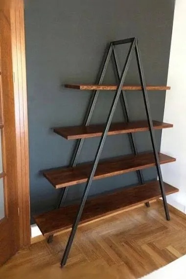 Regał drabinkowy z czterema drewnianymi półkami i metalową, czarną konstrukcją w kształcie litery A, ustawiony na parkiecie w pomieszczeniu z szarą ścianą.