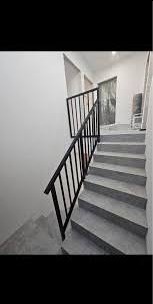 Nowoczesne schody betonowe z czarną, metalową barierką o minimalistycznym designie, widziane z dołu. Białe ściany i szare stopnie tworzą kontrast z ciemną konstrukcją. Ujęcie z perspektywy dolnej...