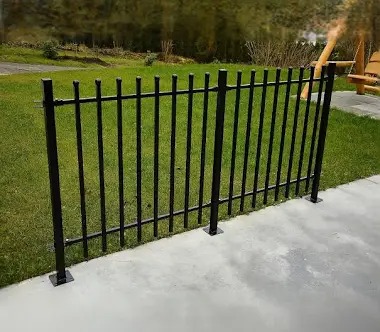 Czarne, metalowe ogrodzenie panelowe na betonowej podstawie, otoczone zielonym trawnikiem i elementami ogrodu w tle.