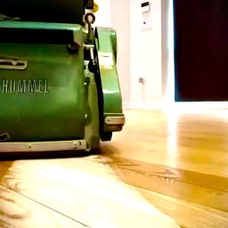 Artur Trembiński - Maszyna Hummel do renowacji podłóg na błyszczącej, odnowionej drewnianej podłodze. Widoczne drzwi w tle.