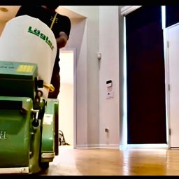 Artur Trembiński - Praca cykliniarką Lagler Hummel na parkiecie w jasnym wnętrzu. Widoczny operator w czarnej koszulce. Podłoga po obróbce ma wysoki połysk.