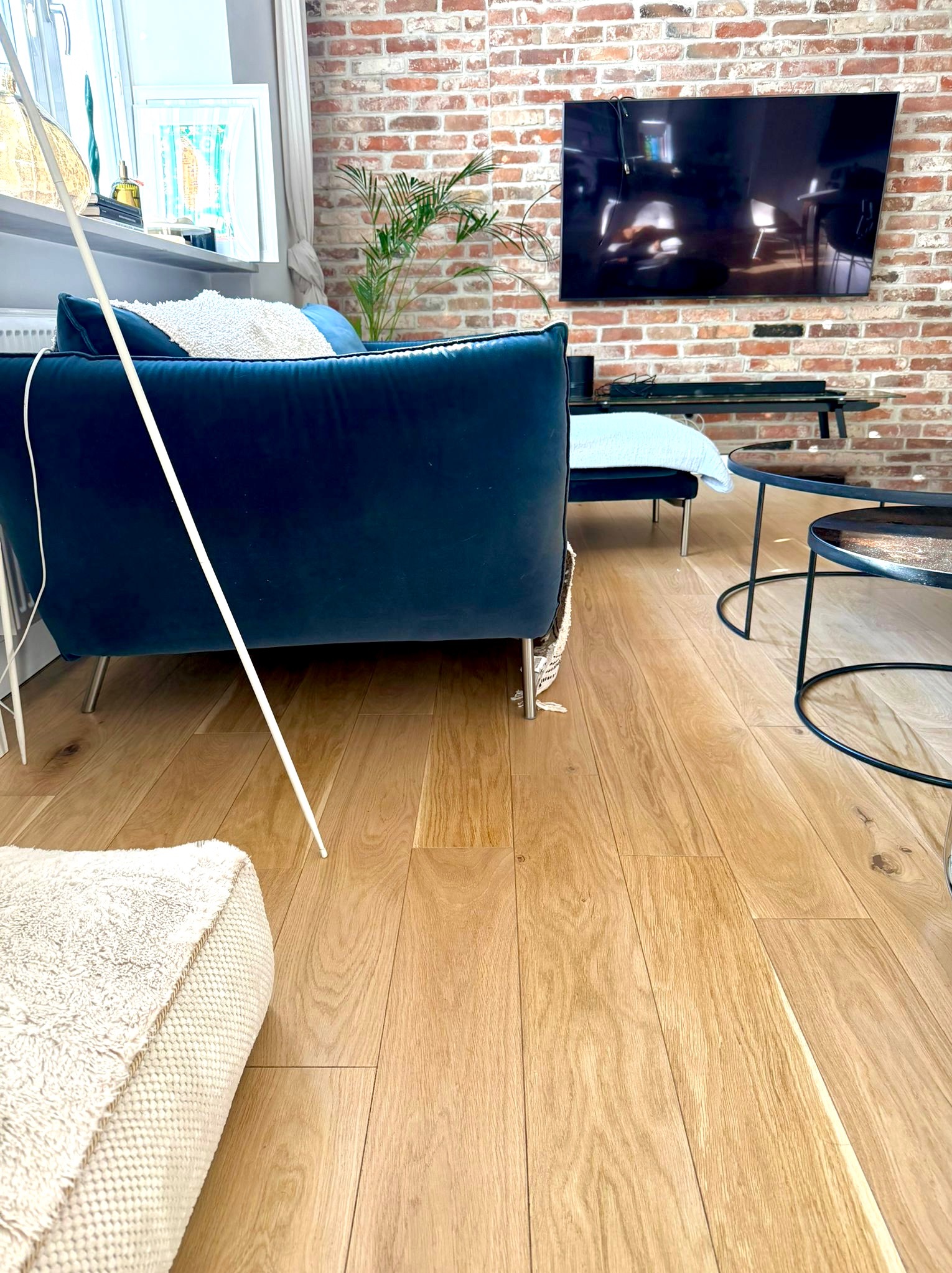 Jasny parkiet w salonie z ceglaną ścianą, nowoczesne meble. Widoczne naturalne usłojenie drewna i subtelne wykończenie podłogi. Minimalistyczny design wnętrza.