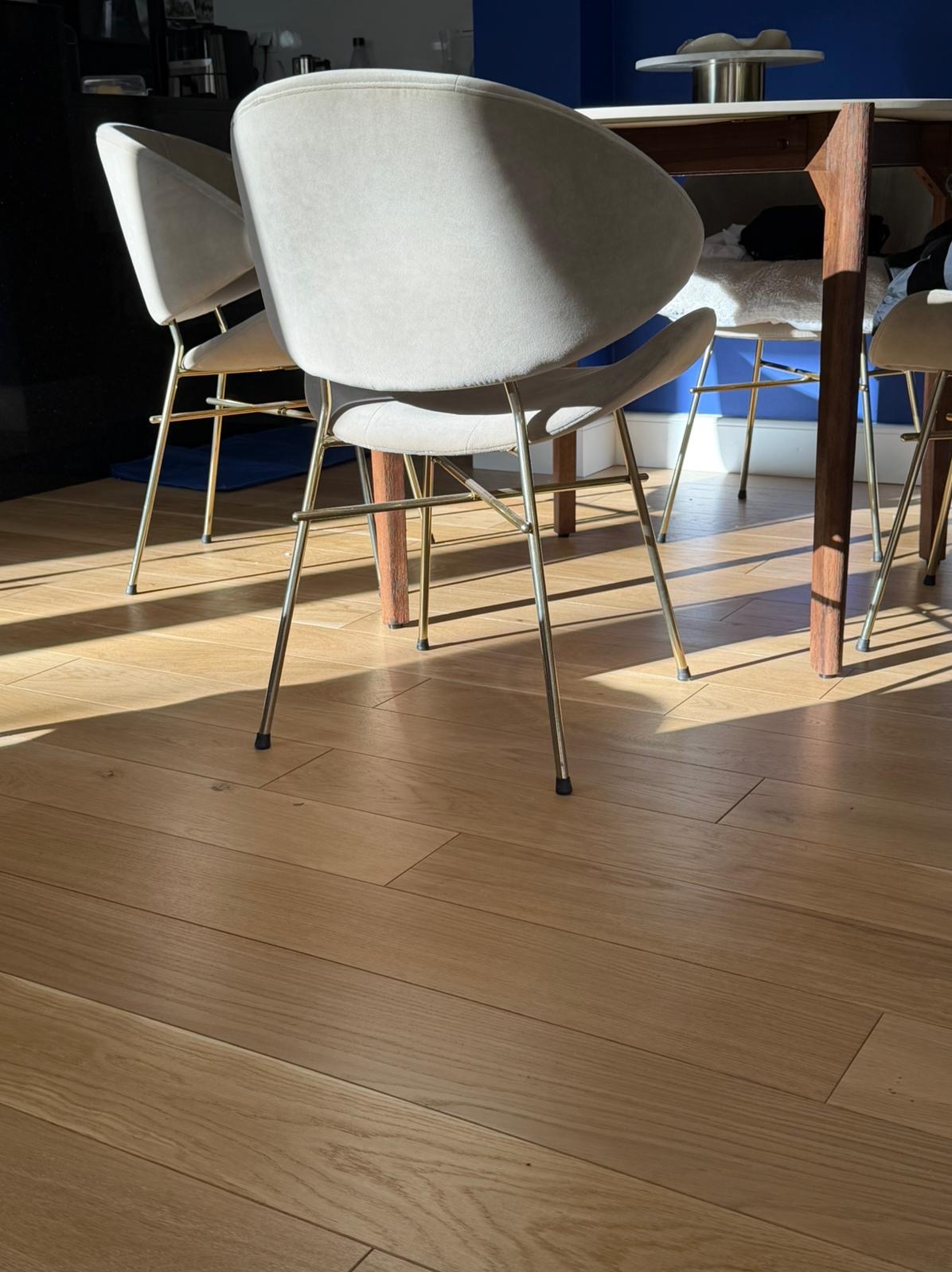 Parkiet w jadalni z krzesłami w stylu retro, oświetlony promieniami słońca. Jasne drewno i minimalistyczny design tworzą ciepłą atmosferę.